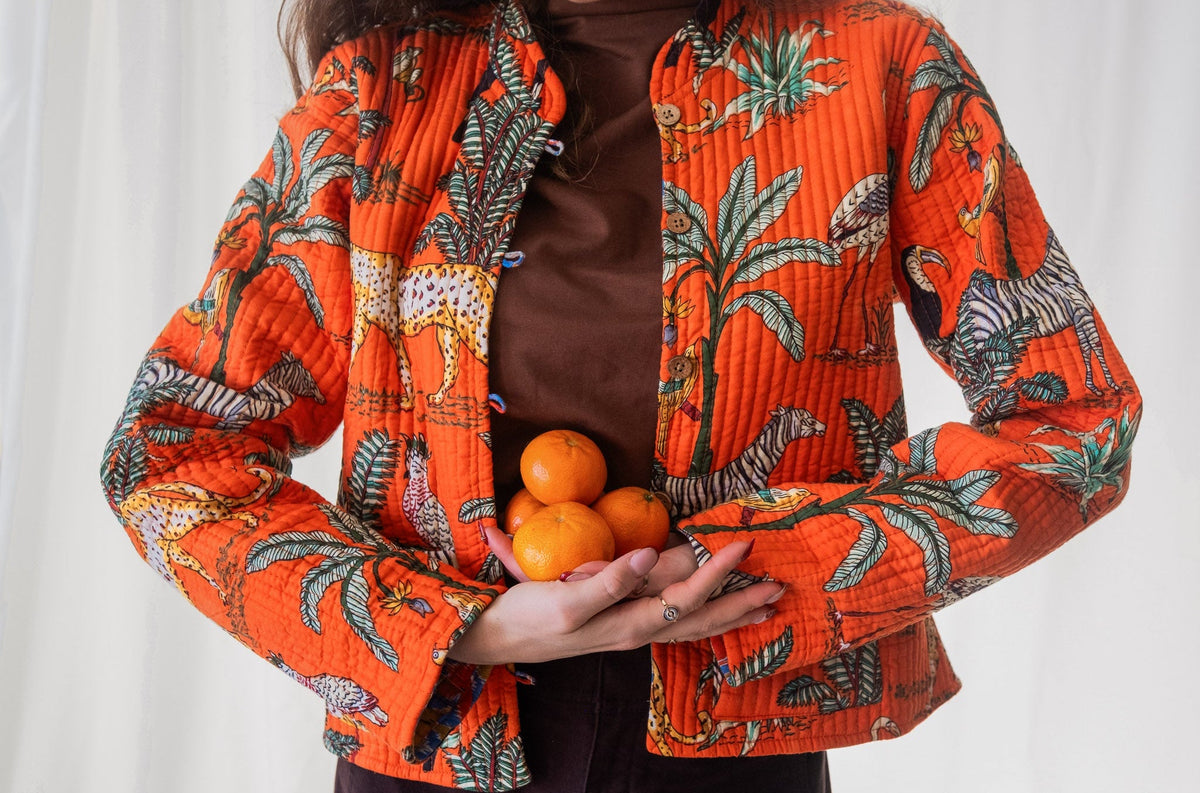 Person wearing an orange patterned jacket holding oranges against a white background